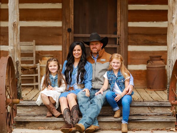 Smiling family dressed in western attire sitting on rustic wooden porch steps.