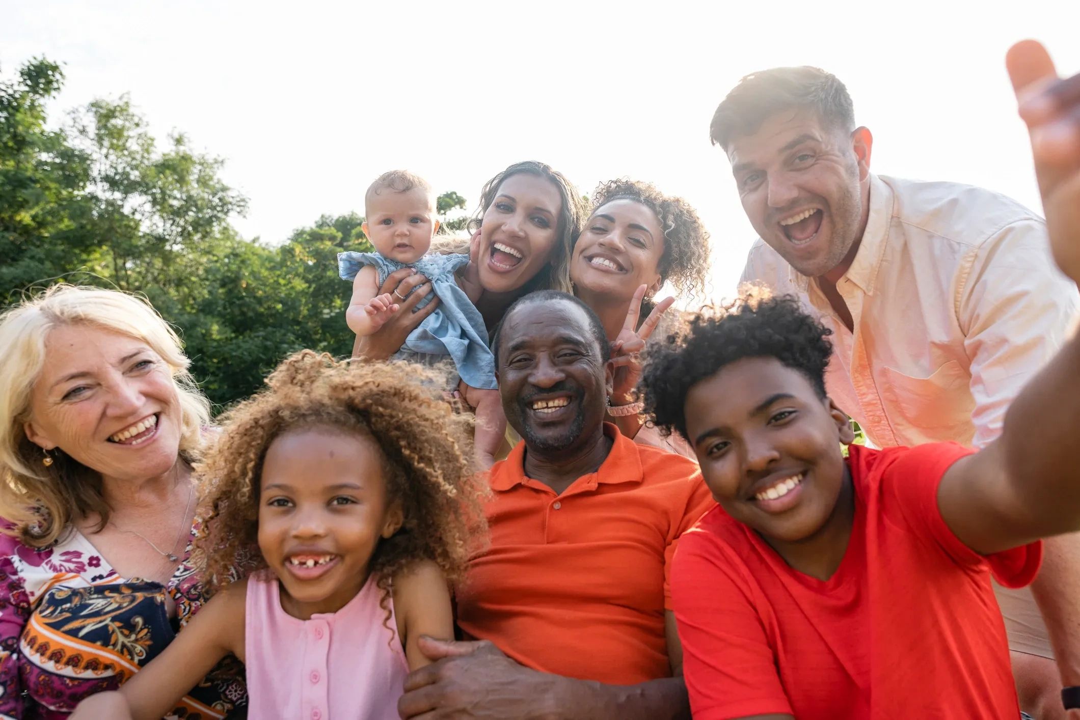 Multi-generational family smiling outdoors for a selfie.