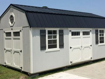 A white and gray barn-style shed with black roof and shutters on a grassy lawn.