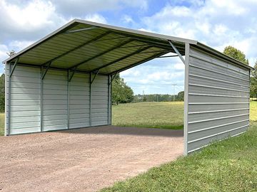 Metal carport shelter with three walls on a grassy area.