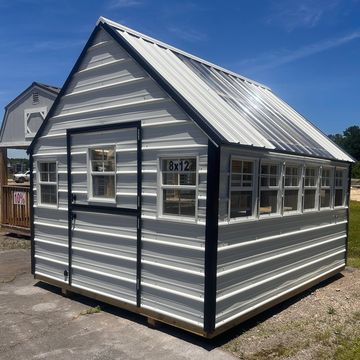 Metal greenhouse with multiple windows and a translucent roof panel under a clear blue sky.