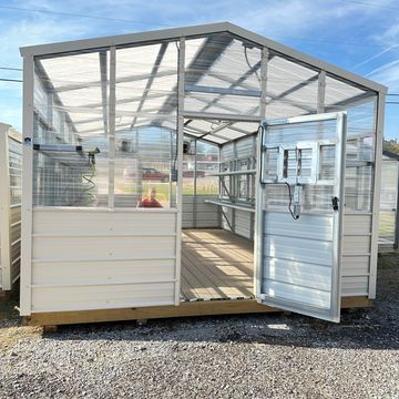 Metal and polycarbonate greenhouse with open door on gravel.
