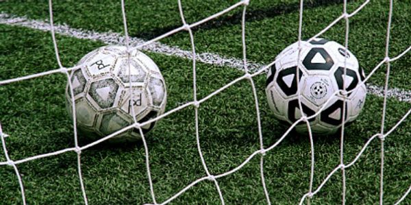 Two soccer balls caught inside a goal net on a green field.