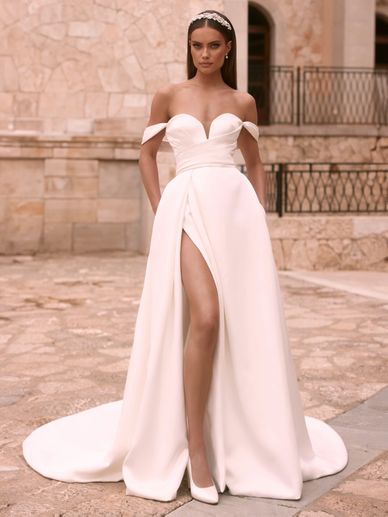 Elegant woman in an off-shoulder white gown with a thigh-high slit and headband.