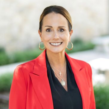 Confident woman in red blazer smiling outdoors.