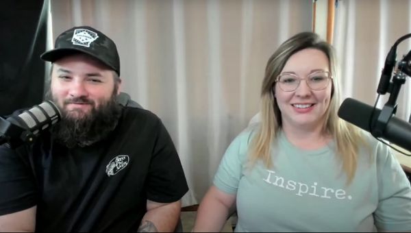 Two people smiling on a podcast or live stream with microphones.
