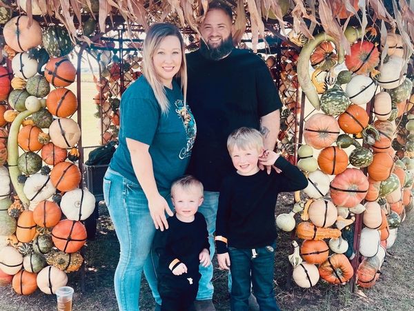 Family of four posing under a decorative arch made of autumn gourds and leaves.