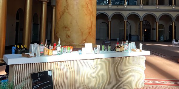 Modern bar setup with various liquor bottles on a white counter and elegant wavy wall design.