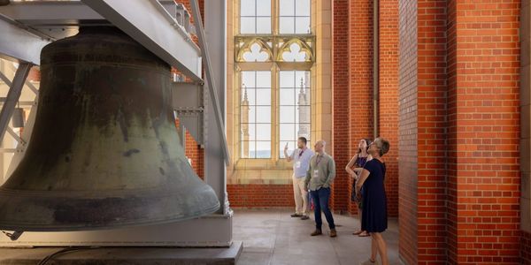 People observing a large historic bell inside a brick tower.