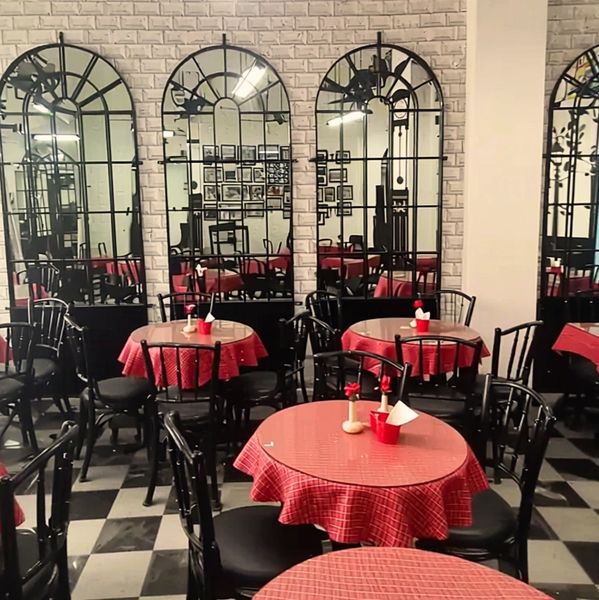 Restaurant interior with red-checkered tablecloths and black chairs reflected in large arched mirrors.