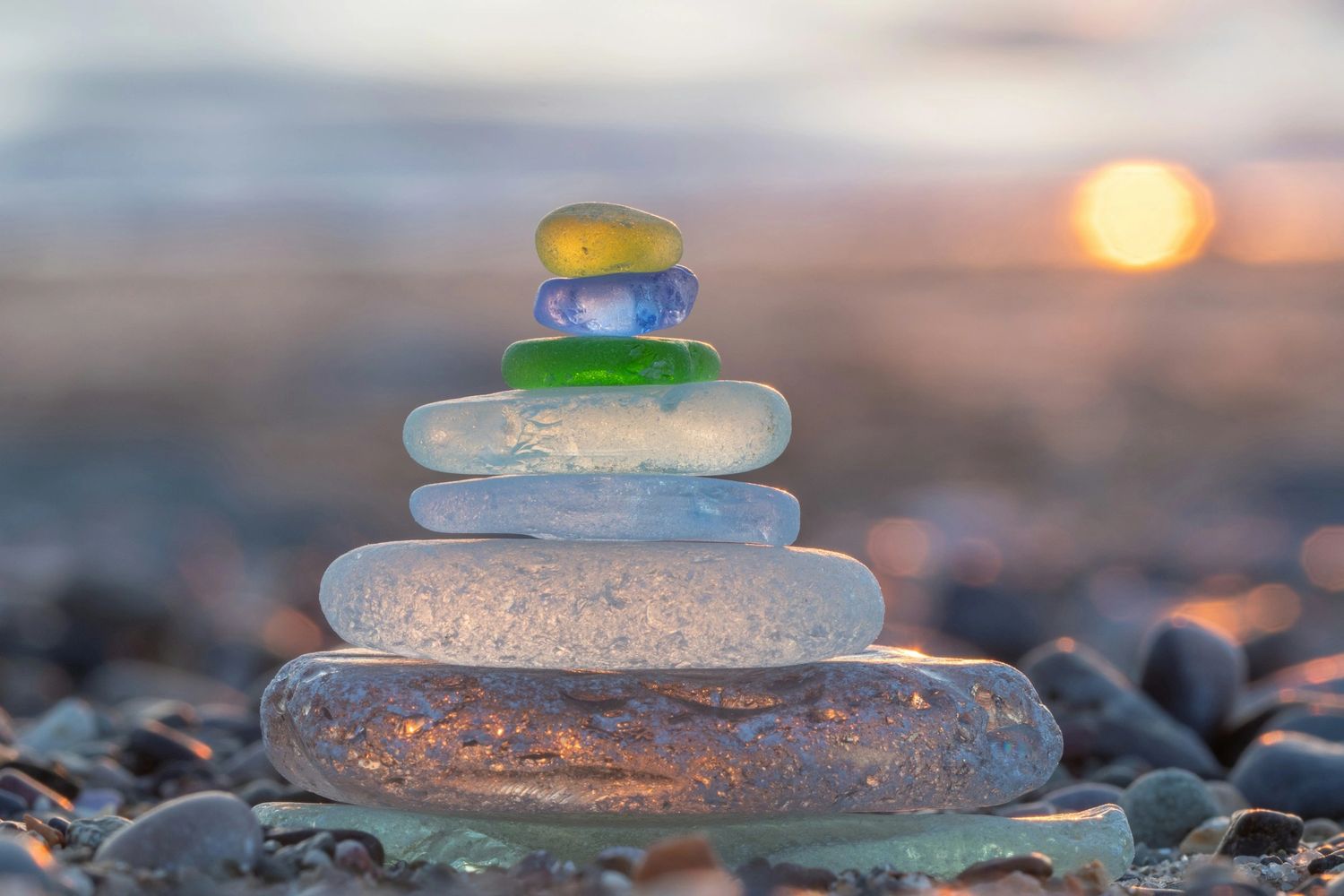 Stack of colorful sea glass pieces glowing at sunset on a beach.