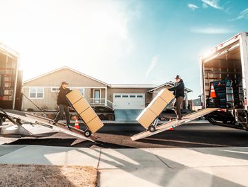 Two Moving Trucks with Movers exiting ramp with boxes on handtruck