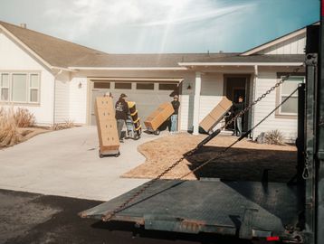 Four movers with hand trucks, carrying moving boxes, up the driveway and into home