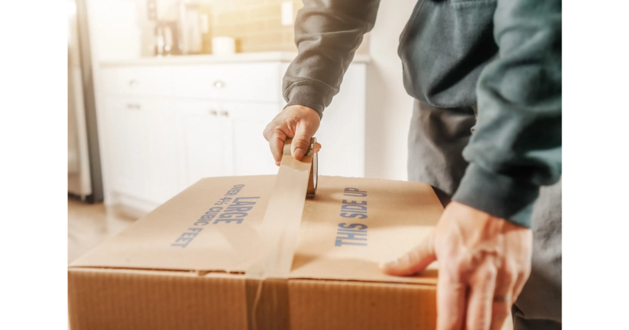 Bend Brothers Moving Company Mover in Kitchen taping a moving box closed.