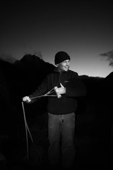 Man in outdoor gear playing with a slingshot at dusk.