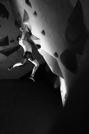 Man climbing an indoor rock wall, captured mid-move.