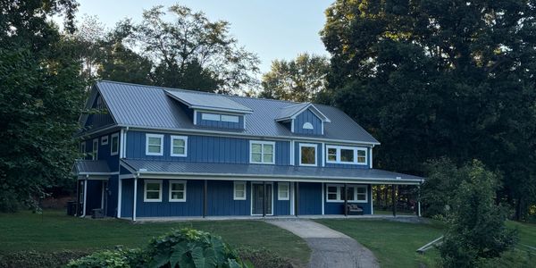 A large blue house with a metal roof surrounded by trees.