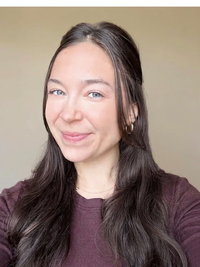 Smiling woman with long brown hair and blue eyes wearing a purple top.