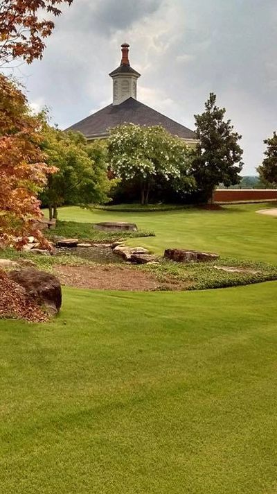 Landscaping with green grass and a building with a shingled roof in the background