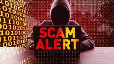mysterious hooded figure behind a laptop with the words scam alert highlighted.