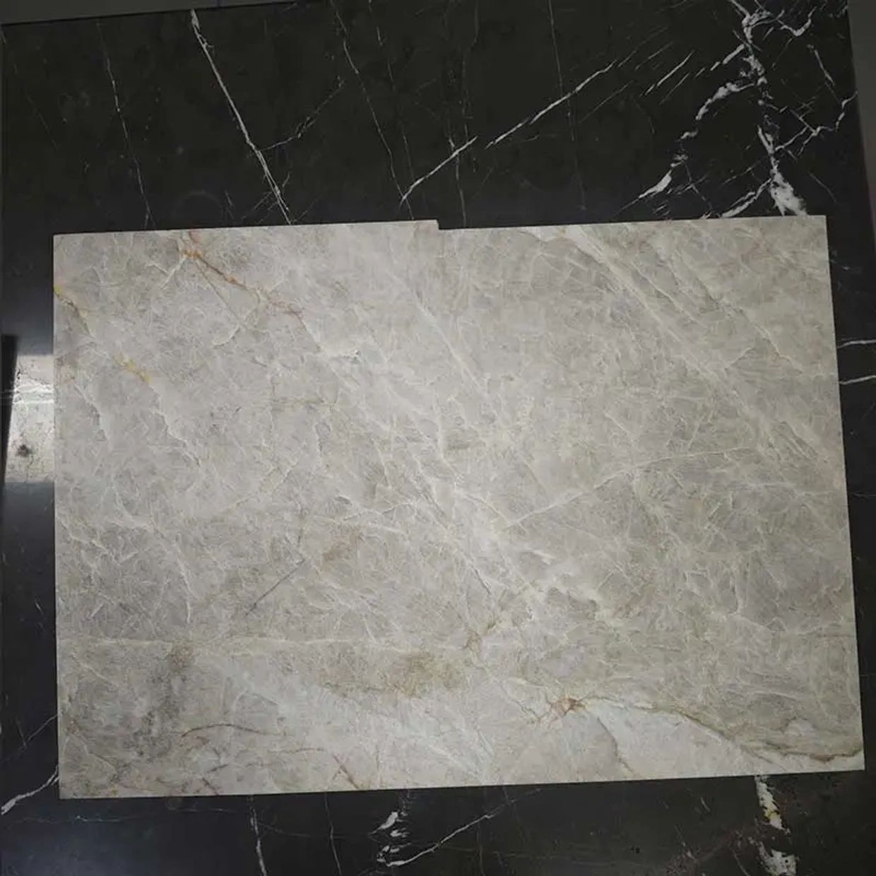 A rectangular beige marble slab on a black marble surface.