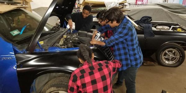Young adults in the auto shop working on an engine.