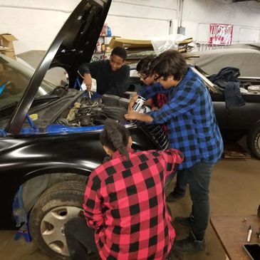 Young adults in the auto shop working on an engine.