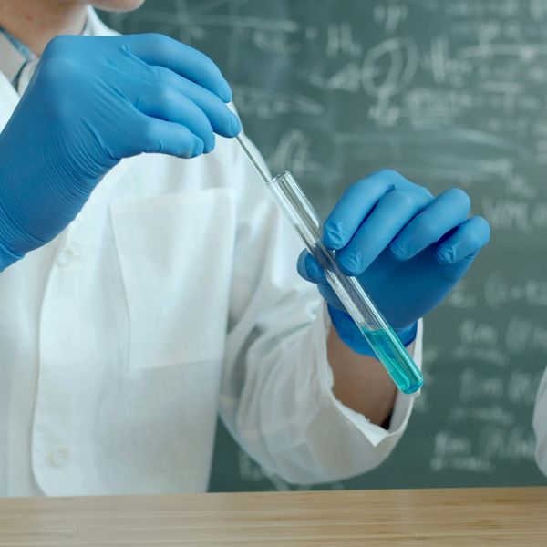 A scientist putting a long swab into a test tube with green liquid.