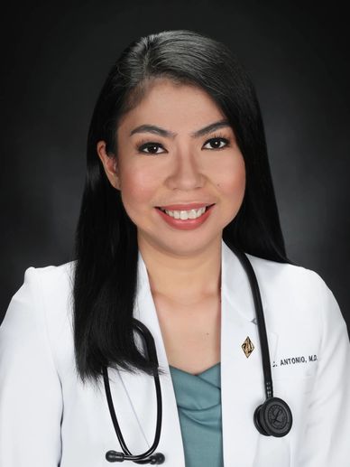 Smiling female doctor in white coat with stethoscope against dark background.