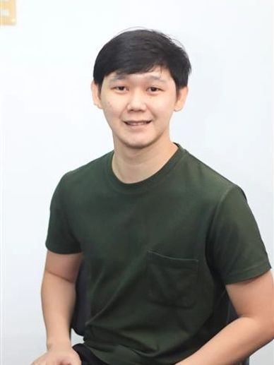 Young man in a dark green t-shirt sitting and smiling.