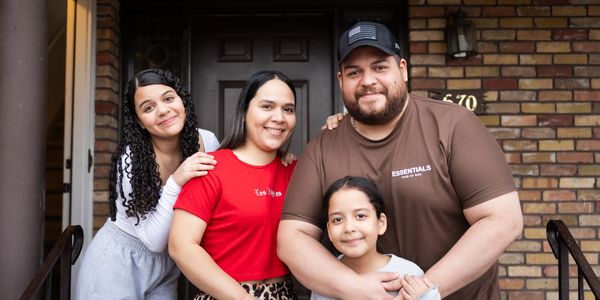 Happy family of four posing outside their home, smiling warmly.