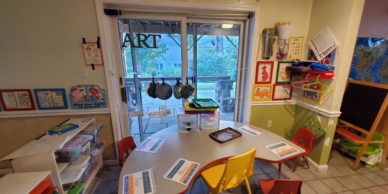 A colorful art classroom setup with children's chairs and tables near a sliding glass door.
