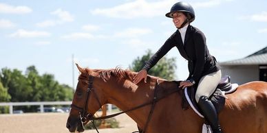 Smiling rider petting a brown horse.