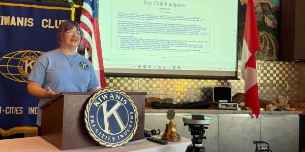 Person speaking at a Kiwanis Club event with flags.