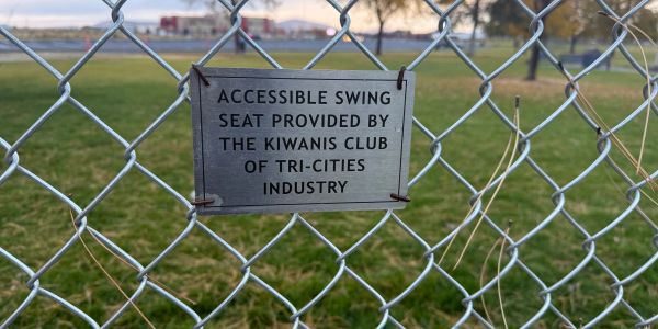 Sign on chain-link fence about accessible swing seat.