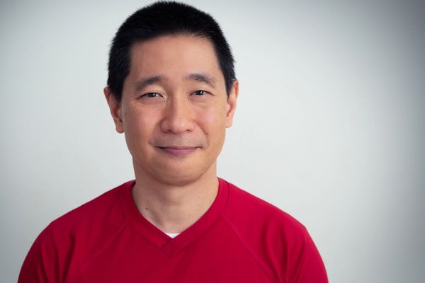 Smiling man in a red shirt against a plain background.
