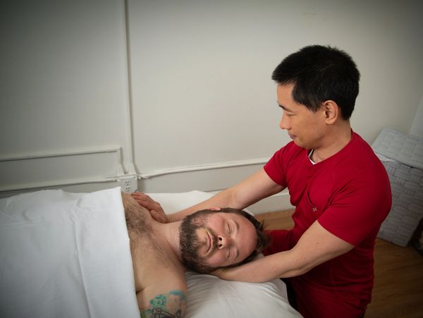 A massage therapist works on a patient's neck and shoulders. The patient is in a supine position.