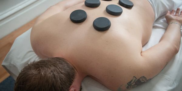 A person lies on a massage table facing down. Six therapeutic hot stones are placed on his back.