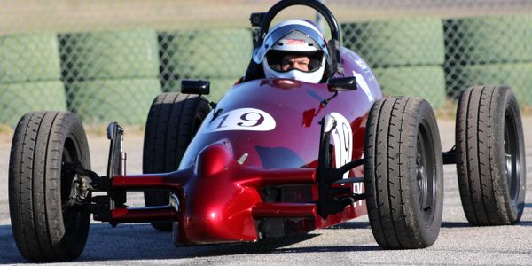 A person driving a vintage red race car on a track.