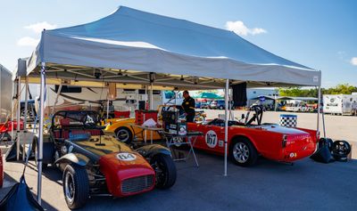 Two vintage race cars parked under a canopy at a racing event.