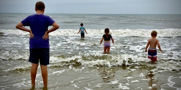 Four children wading into the ocean on a cloudy day.