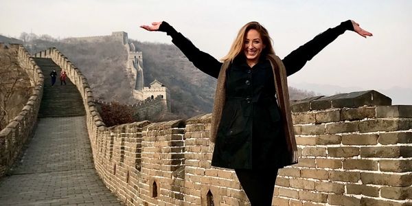 Woman joyfully posing on the Great Wall of China with arms raised.