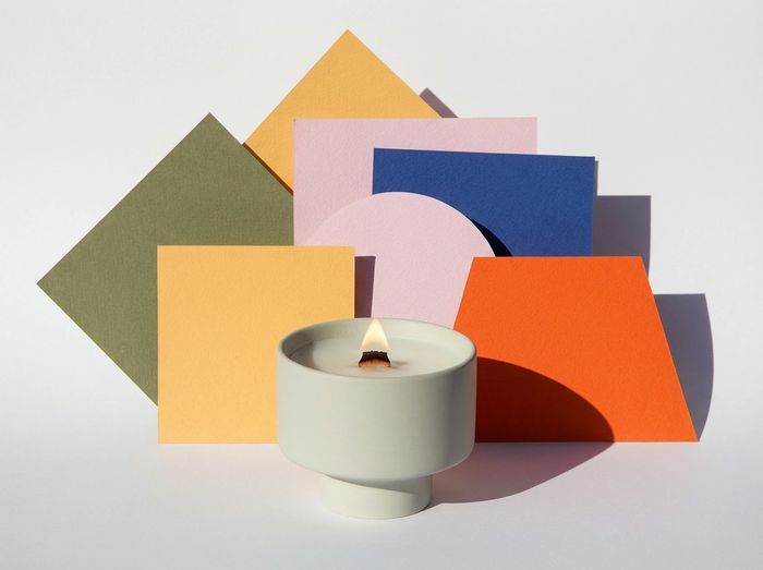 Minimalist candle with colorful geometric shapes in the background.