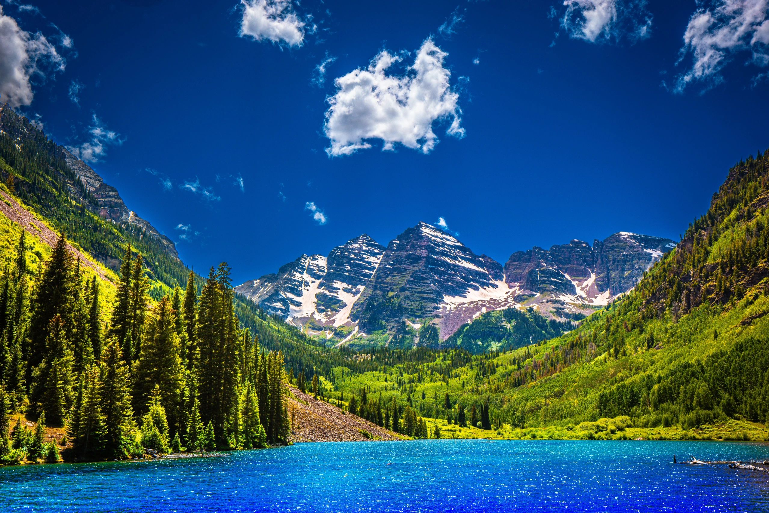 Snow-capped mountains overlooking a bright blue lake with lush greenery.