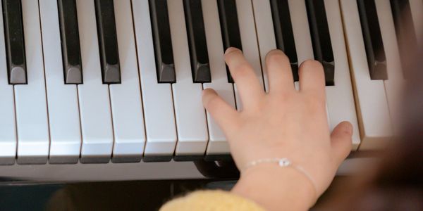 Child's hand playing piano keys with focus on fingers.