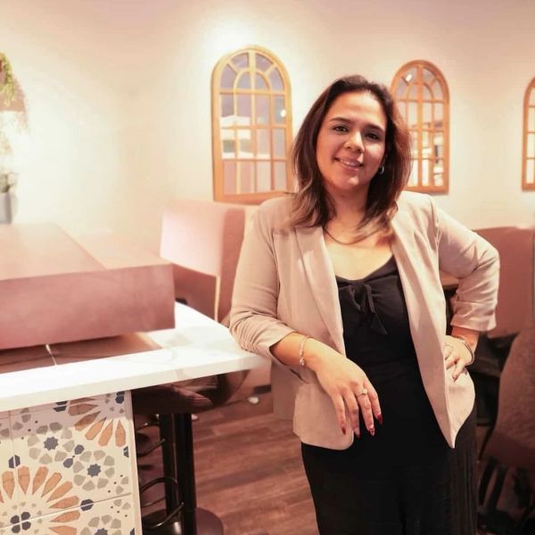 Woman in a blazer smiling indoors near decorative mirrors.