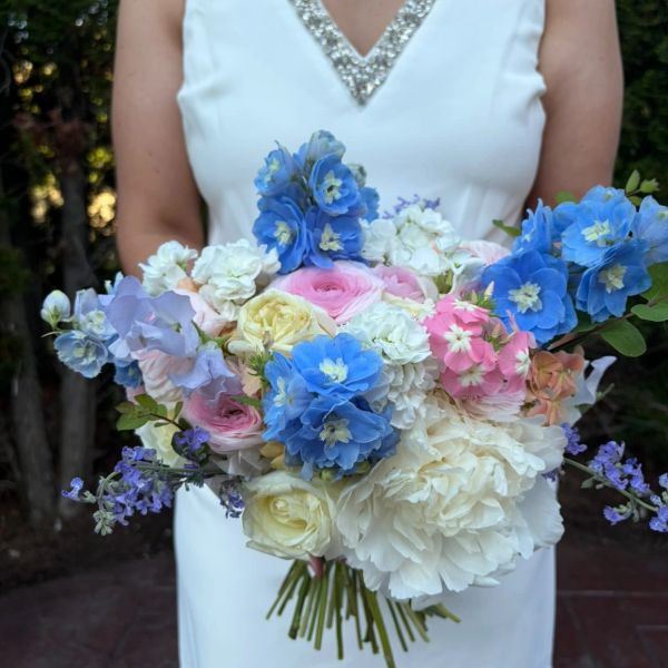 Bride holding a colorful bouquet of blue, pink, and white flowers.