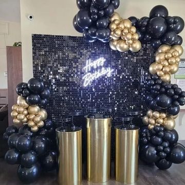 Elegant black and gold balloon birthday decoration with a shiny backdrop.