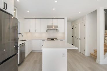 Modern white kitchen with island and stainless steel appliances.