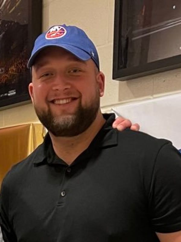Man smiling in a blue cap and black polo shirt.